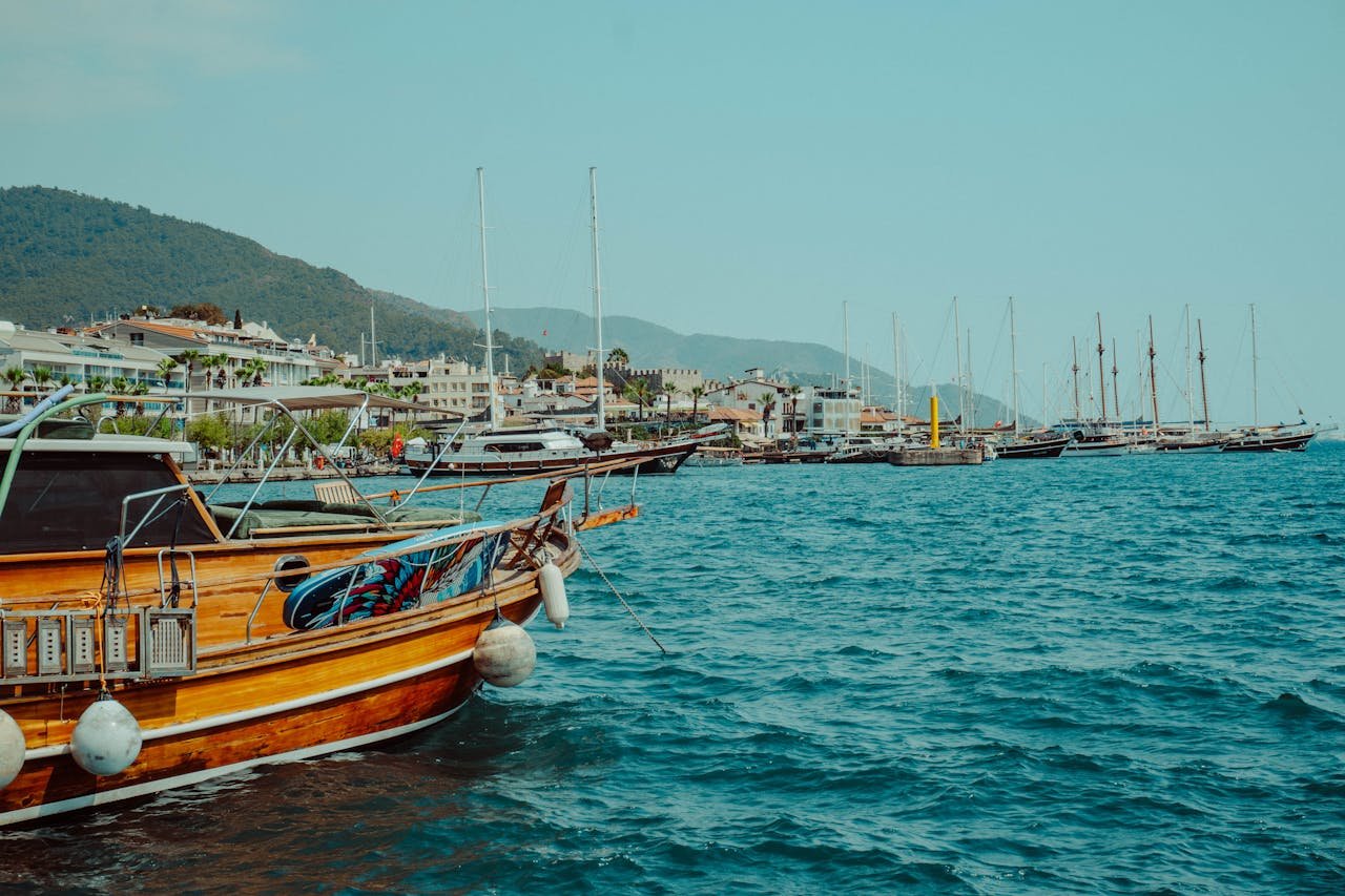 A picturesque view of sailing boats docked at a Mediterranean seaside with mountains in the background.